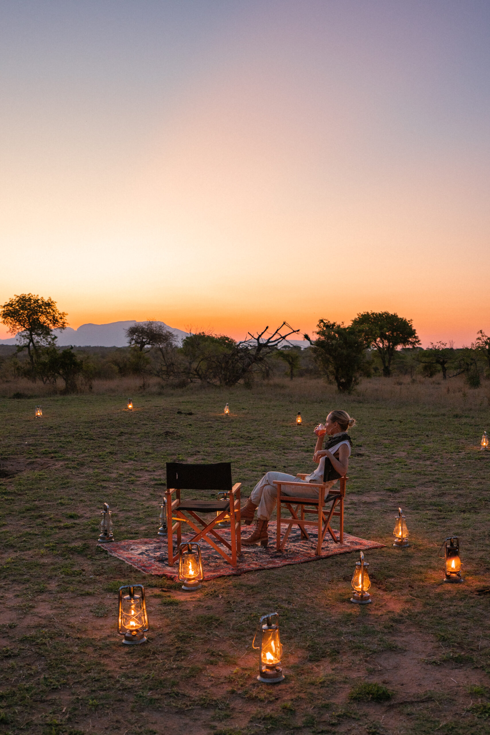 salty luxe enjoying a drink at sunset in kruger national park with lanterns all around her