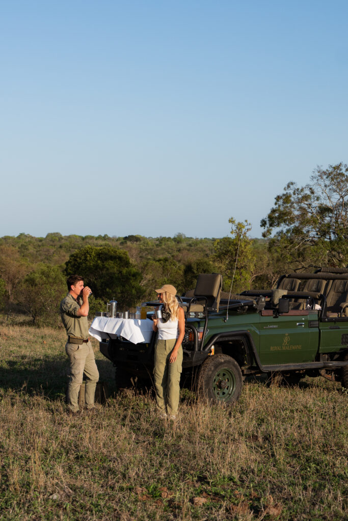 a couple standing in front of a safari vehicle in kruger national park and having a drink