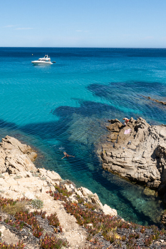 white boat in blue water with a woman swimming between the rocks