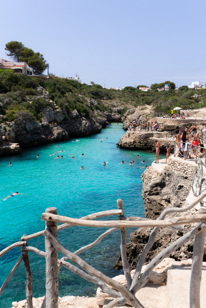 people swimming and standing on the platforms at cala en brut, one of the best beaches in menorca