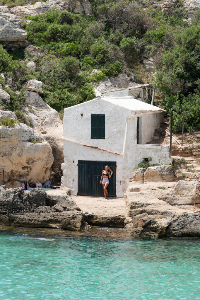 a woman standing in front of a white washed building at cala binidali menorca