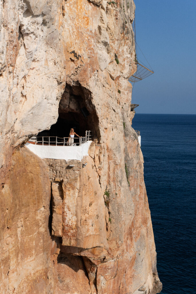 A woman looking out of a hole in the cliff at Cova d'en Xoroi in Menorca