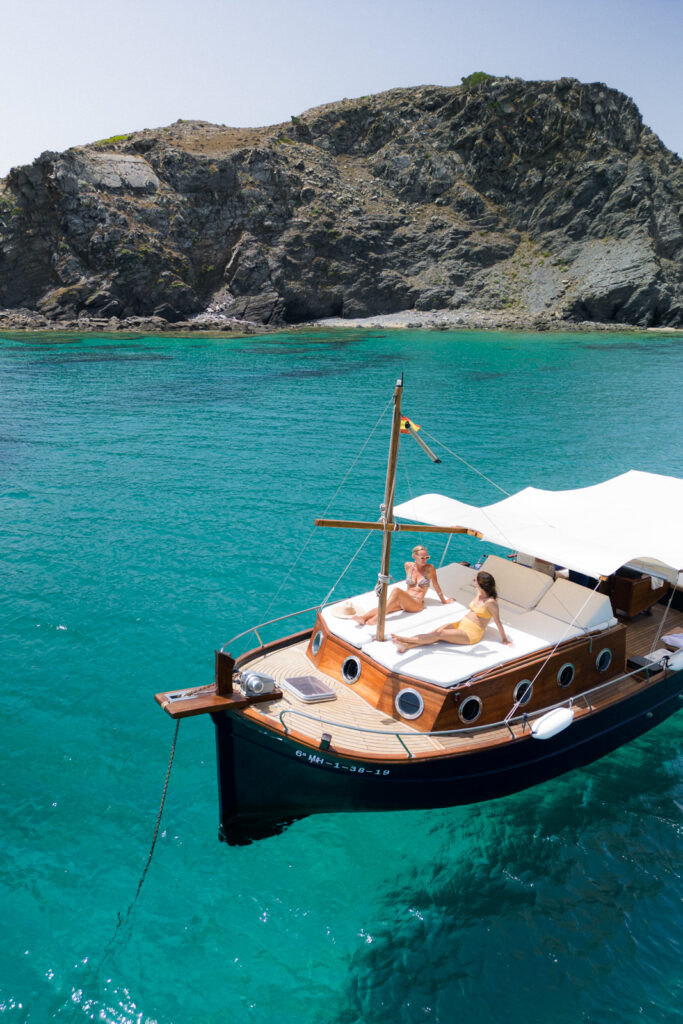 two woman sunbathing on a boat tour in menorca on a traditional wooden boat