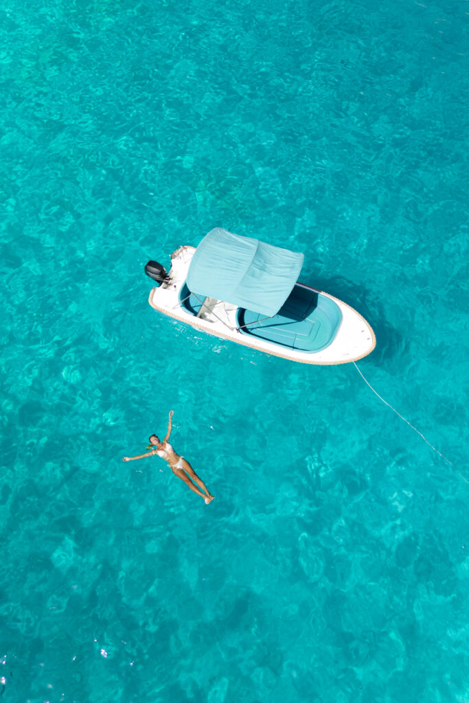 Salty Luxe floating next to a boat in the clear blue waters of Menorca