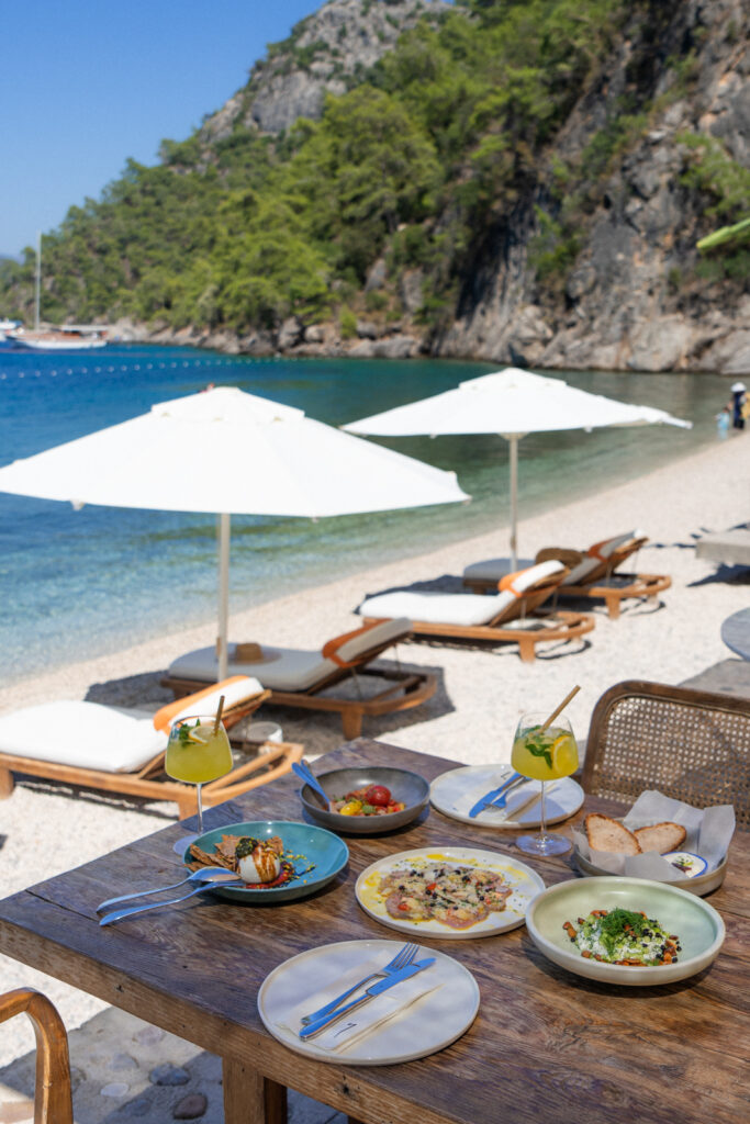 beach umbrellas and a meal on the table overlooking the beach at yazz collective fethiye