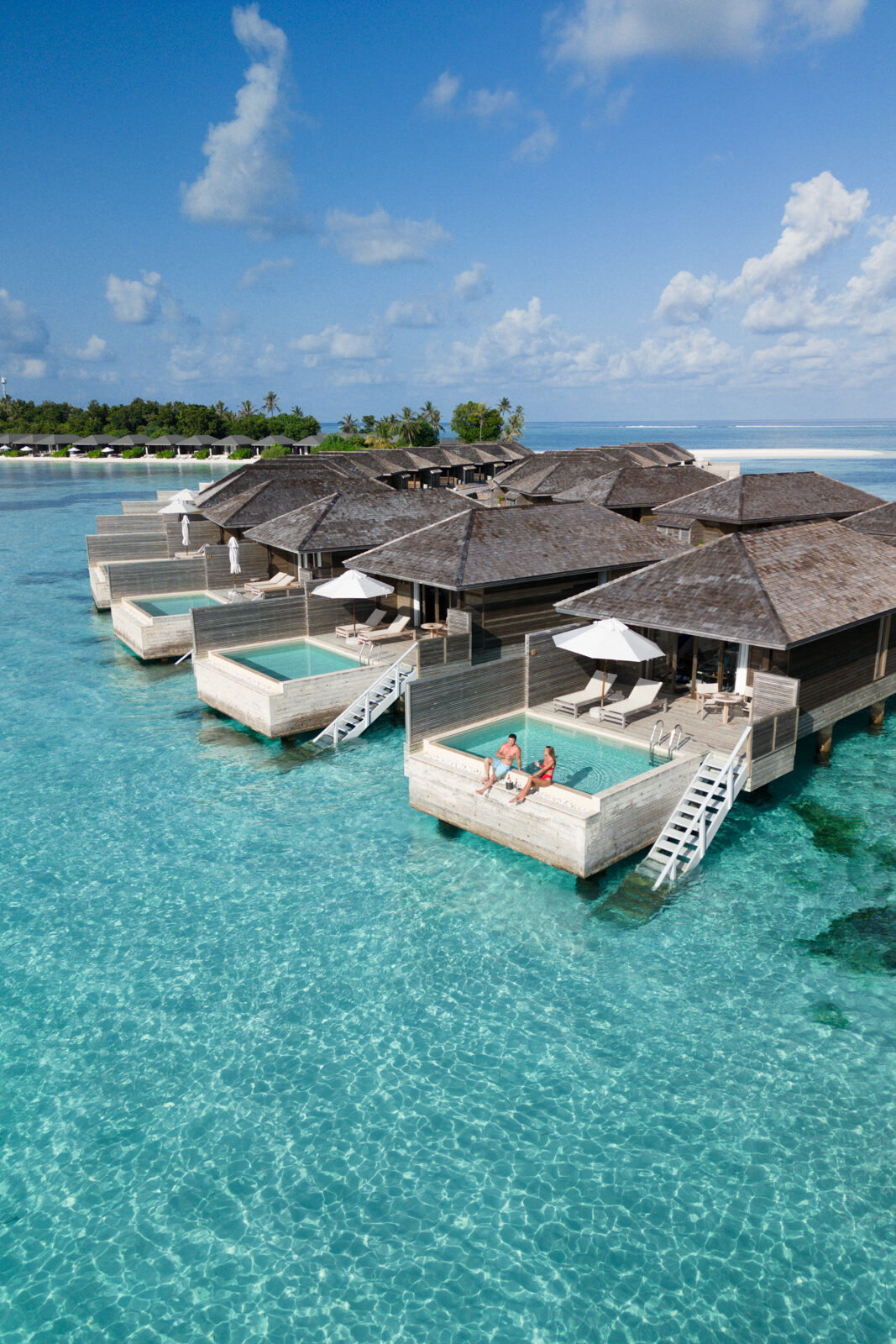 A couple sitting on the edge of a private pool overwater bungalow at Jawakara Maldives, an affordable luxury hotel in the Maldives